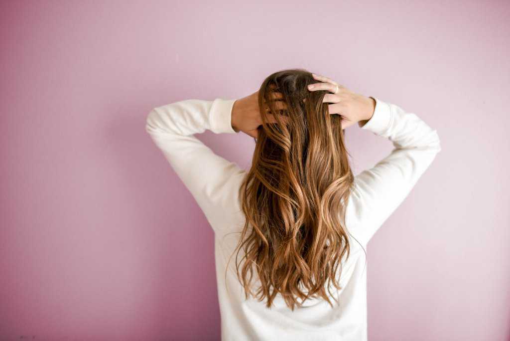 a woman with long brown hair standing in front of a pink wall.