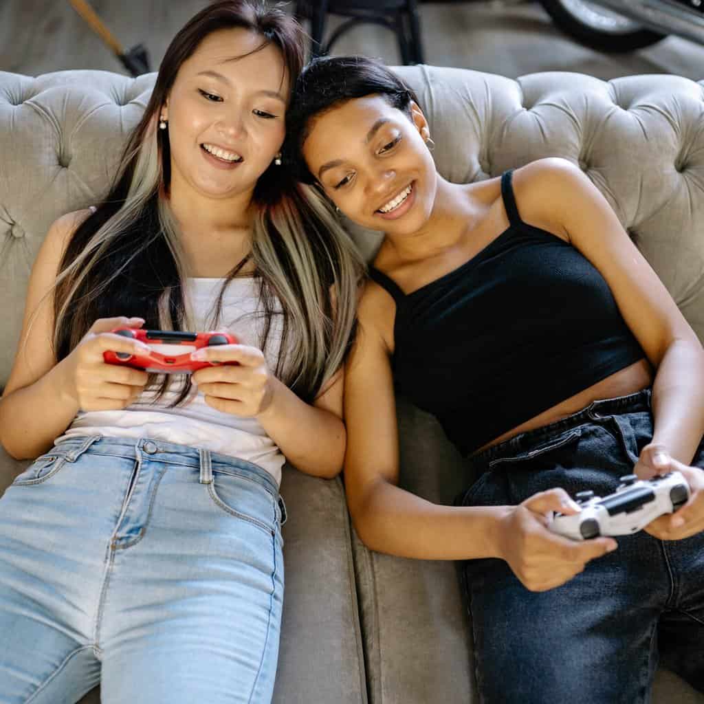 two women sitting on a couch holding remotes.