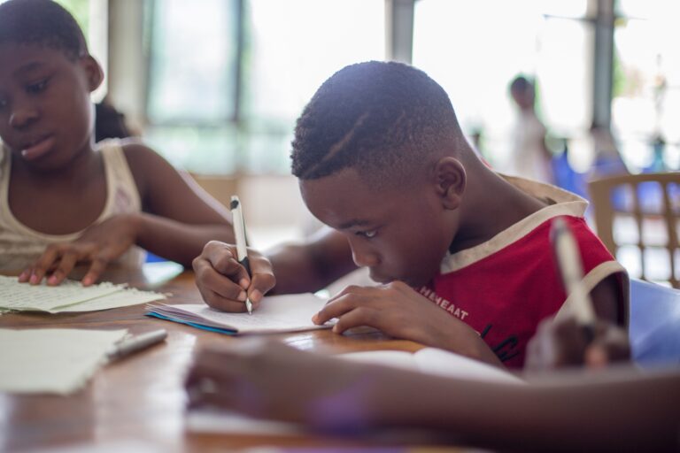 a group of children sitting at a table and writing in a notebook.