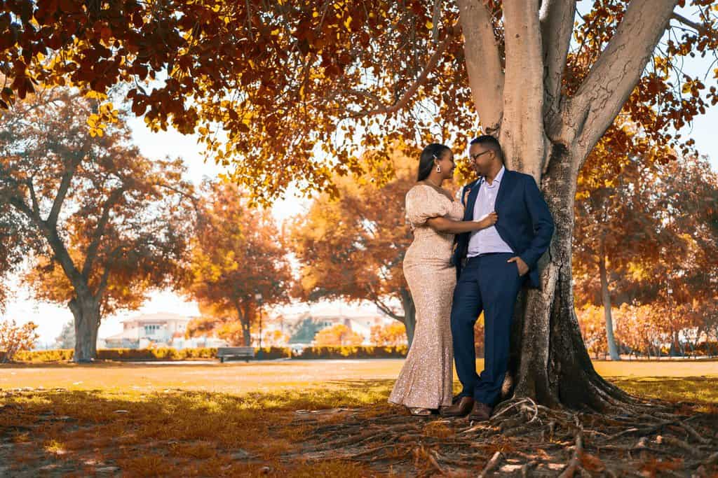 a couple is leaning against a tree during their engagement session.