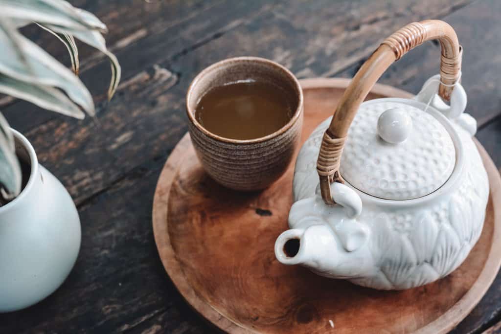 a white teapot sits on a wooden tray with a cup of tea.