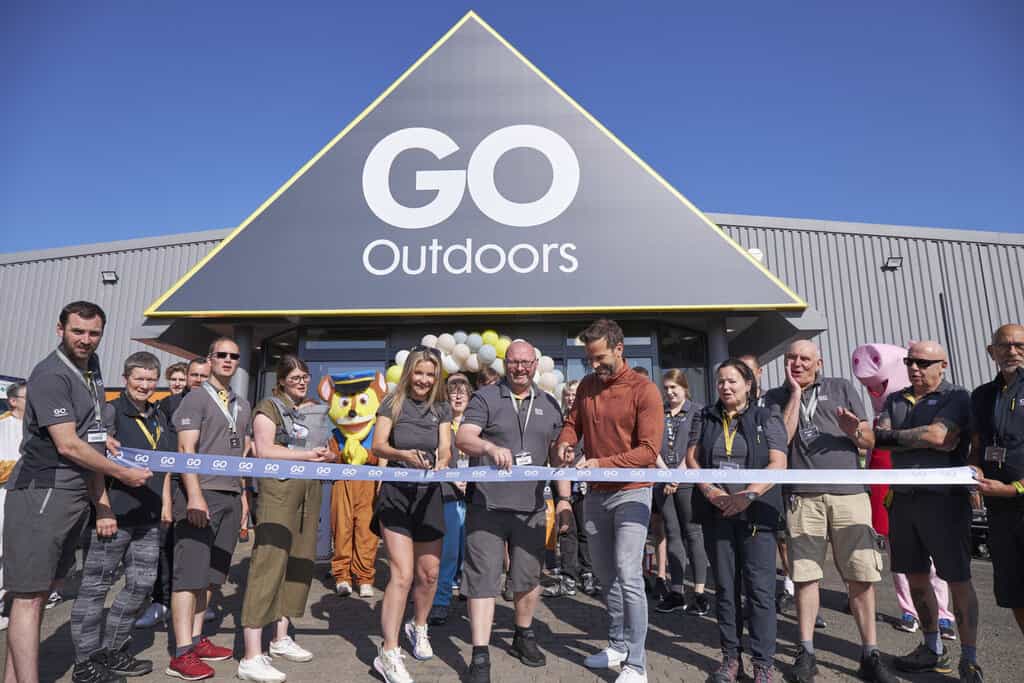 a group of people cutting a ribbon in front of a go outdoors store.