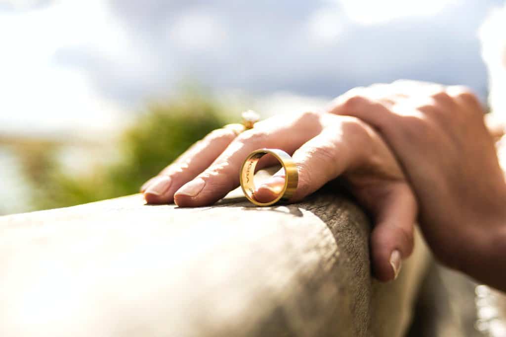 A woman's hand holding a gold wedding ring.