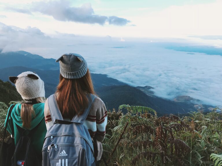 Two women standing on top of a mountain overlooking the clouds.