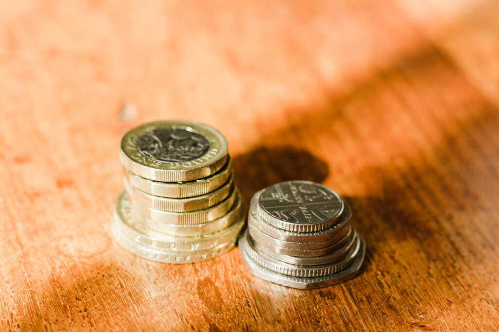 A stack of monthly pound coin investments on a wooden table, ready to make money.