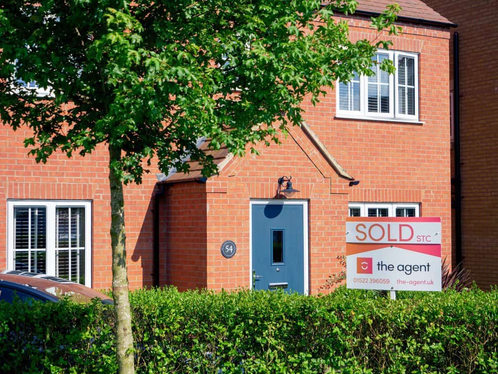 Someone leaving their home, with a sold sign in front of it.