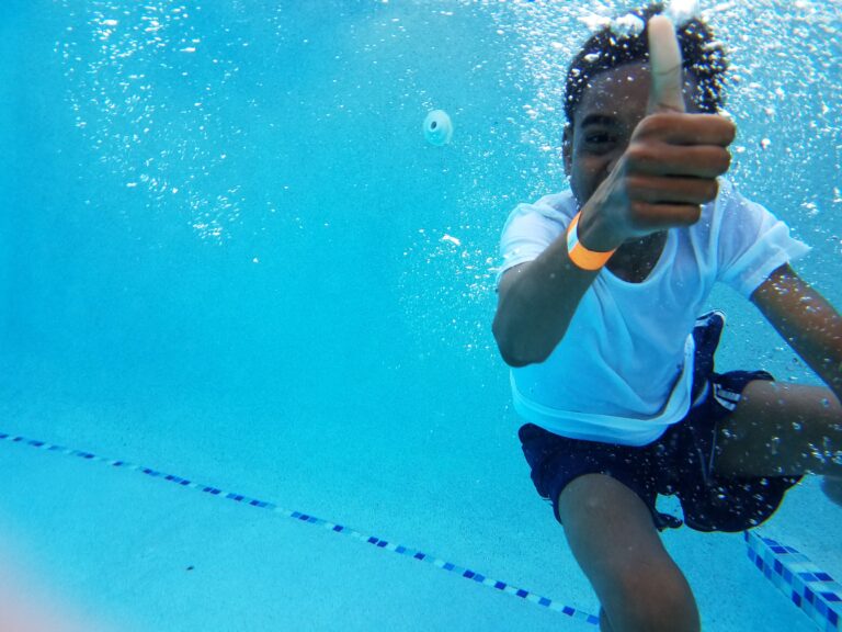 A young boy underwater giving a thumbs up while learning to swim.