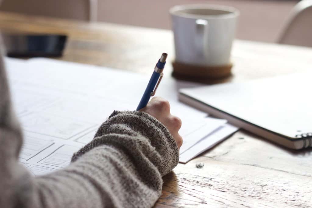 A person writing with a pen on a wooden table to support kids' studies.