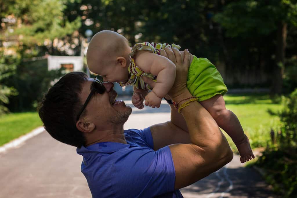 An entrepreneurial parent effectively manages their time while holding a baby up in the air.
