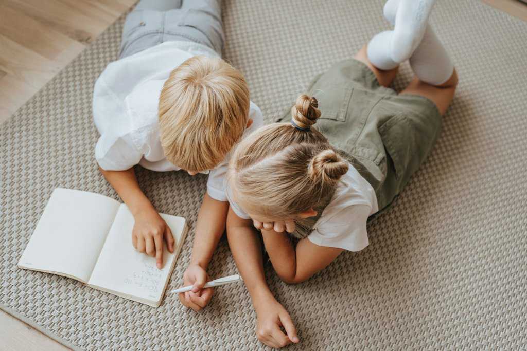 Two children engaged in a routine game on a rug, thriving and winning while writing in a notebook.