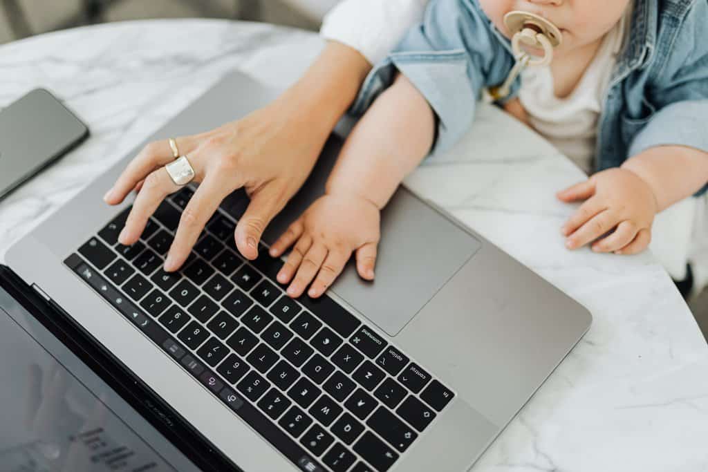 A working mom with a baby on her lap managing work-life balance by typing on a laptop.