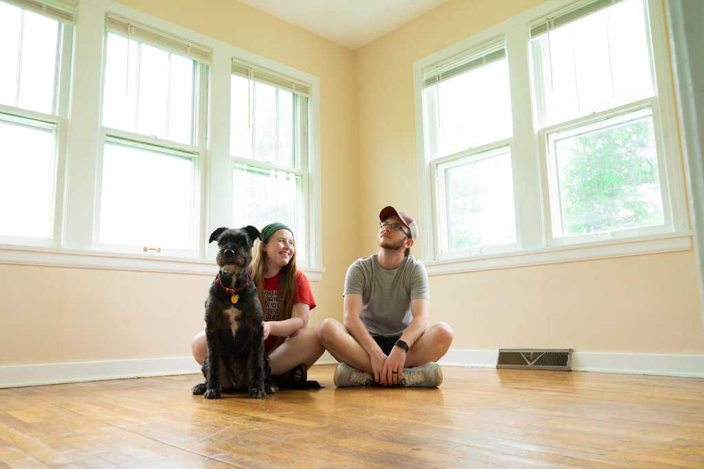 First-time home buyers guide: Two people sitting on the floor with a dog in their family home.