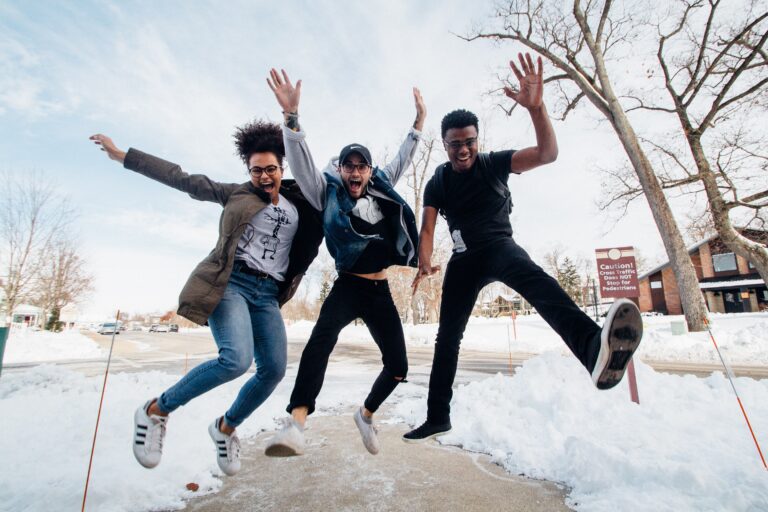 Three young teens prepare to explore new horizons as they joyfully jump in the snow on a sidewalk.