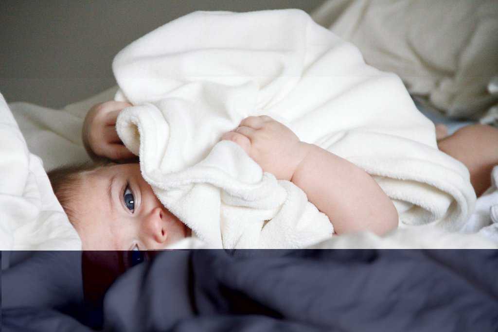 A baby is laying under a blanket, adhering to safe sleep guidelines.
