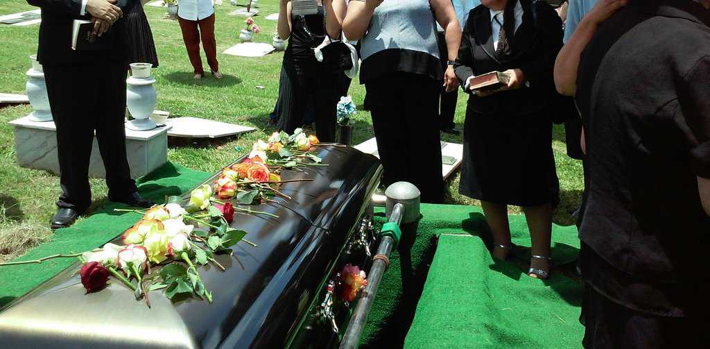 A group of mourners standing beside a flower-adorned urn at a graveside cremation service.