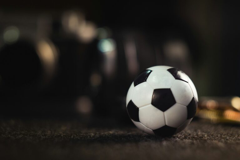 A small soccer ball in focus with a blurry background suggesting other sports equipment related to sports betting.