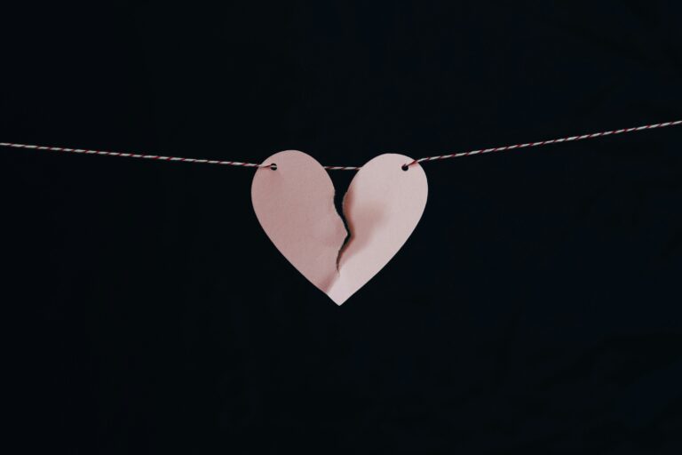 A torn paper heart hangs by a string against a dark background, as if abandoned in an auto draft of forgotten memories.