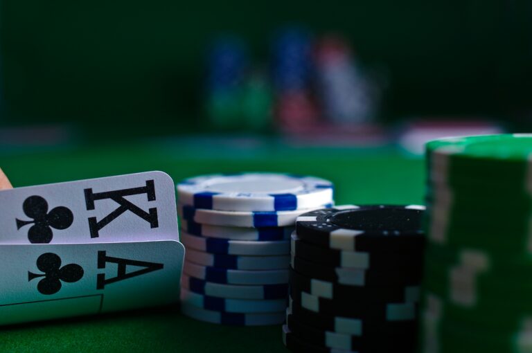 A poker game close-up showing a player's hand with the King and Ace of Clubs, and stacked poker chips on a green table — hinting at the future of online gambling in virtual reality casinos.