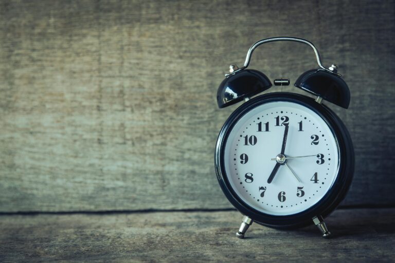 A black vintage alarm clock with a white face and black numerals is placed on a wooden surface against a rustic wooden backdrop, evoking the tranquility before a nightly curfew for Tweens. The time on the clock shows 10:10.